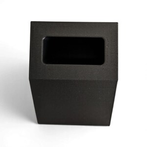 May include: A black, rectangular, open-top container with a textured surface. The container has a rectangular opening at the top and a trapezoidal base. The object is set against a white background.