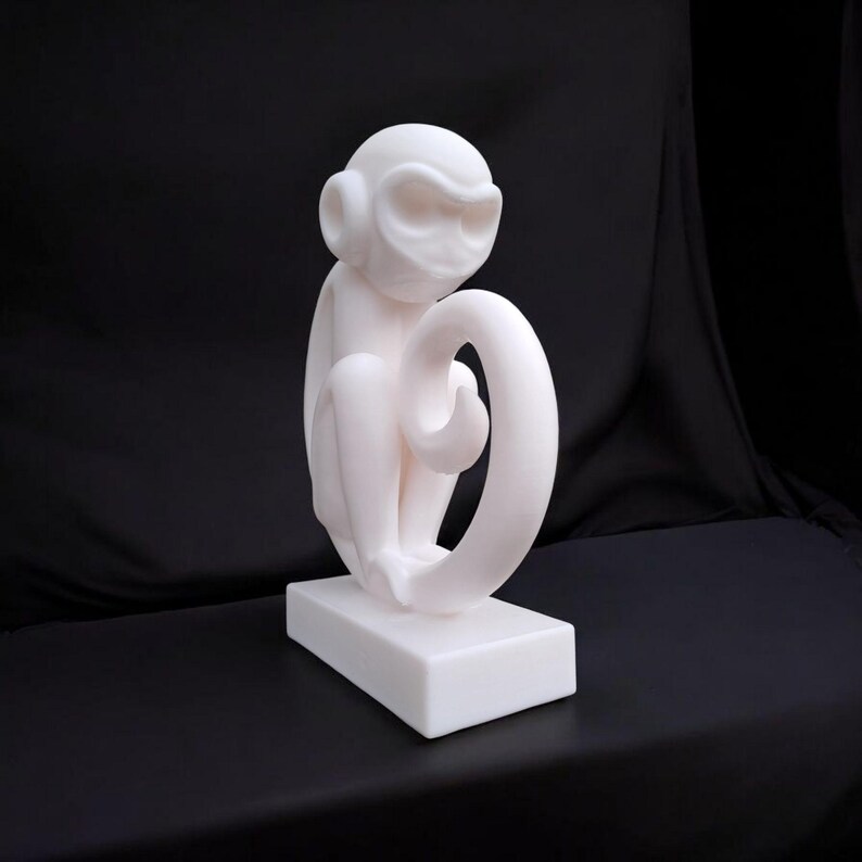 Puede incluir: Escultura blanca de un mono sentado con la cola enroscada. La escultura est&aacute; sobre una base rectangular. El acabado es liso y mate, sobre un fondo negro. Probablemente hecha de resina.