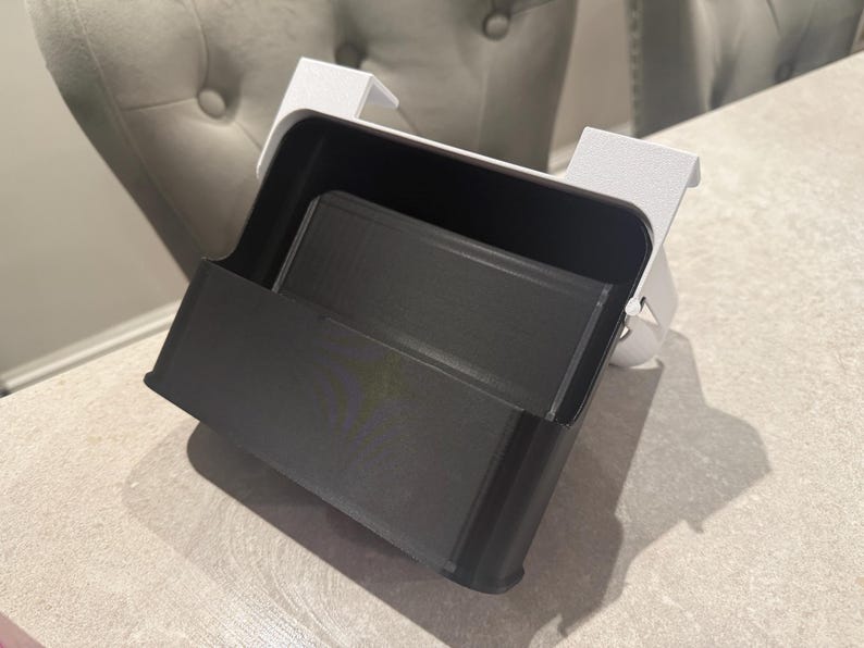 May include: A black and white desk organizer with a rectangular shape. The organizer has a tray and a holder. The organizer is made of plastic and is designed to hold office supplies. The organizer is sitting on a light-colored surface.