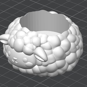 May include: A white, 3D-printed sheep-shaped planter. The planter has a round body with a textured, bubbly surface, and a sheep face with small ears. The interior is hollow, creating a space for plants or other items.