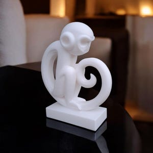 Puede incluir: Una figura de mono blanco con un dise&ntilde;o estilizado. El mono est&aacute; sentado sobre una base rectangular, con su cola formando un bucle. La figura tiene un acabado liso y mate, ideal para la decoraci&oacute;n del hogar.