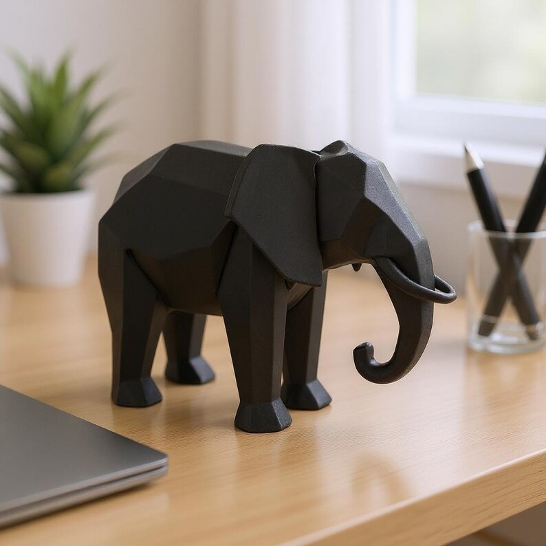 Op de afbeelding: Een zwarte geometrische olifant sculptuur met een slurf en grote oren. De olifant is gemaakt van een solide materiaal en wordt tentoongesteld op een houten oppervlak. De sculptuur is een decoratief item.
