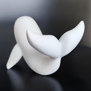 May include: A white whale sculpture with a smooth, matte finish. The whale is depicted in a playful pose, with its tail flukes raised. The sculpture is a minimalist design, perfect for home decor.