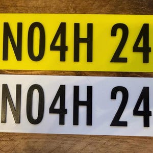 Pu&ograve; includere: Due targhe rettangolari, una gialla e una bianca, ciascuna con il testo nero "N04H 24". Le targhe sono realizzate in un materiale solido e sono esposte su una superficie di legno.