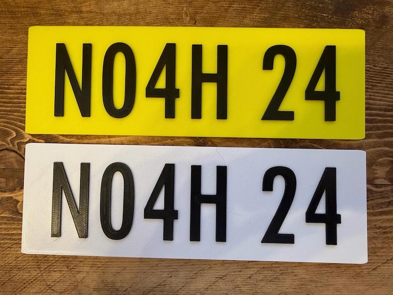 Pu&ograve; includere: Due targhe rettangolari, una gialla e una bianca, ciascuna con il testo nero "N04H 24". Le targhe sono realizzate in un materiale solido e sono esposte su una superficie di legno.