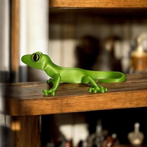 May include: A bright green gecko figurine with a curved tail and detailed legs. The gecko has a small, round head with a dark eye and is positioned on a wooden shelf. The figurine is a decorative item.