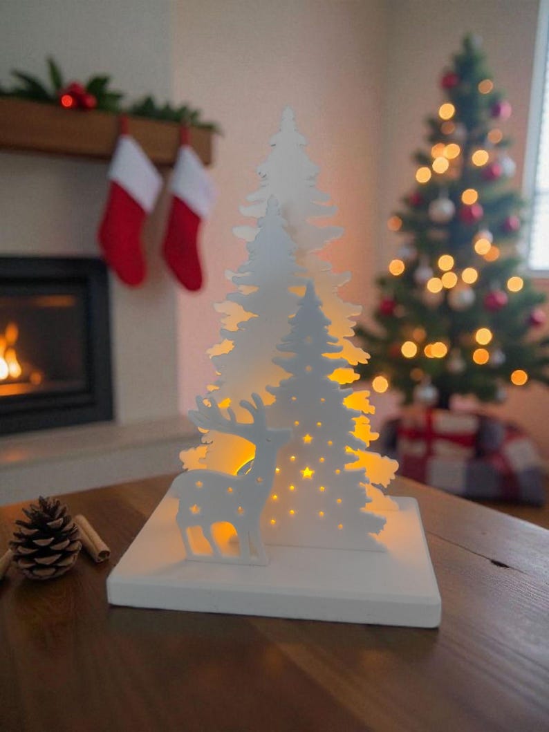 May include: A white Christmas-themed decorative light featuring a deer and a stylized tree design. The tree has star cutouts and is illuminated with warm yellow lights. The light sits on a white base, perfect for holiday decor.