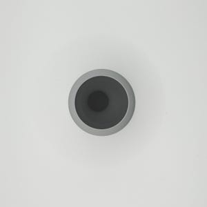 May include: A top-down view of a gray ceramic vase with a dark gray interior. The vase has a rounded shape with a wide opening and a smooth, matte finish. The background is plain white.