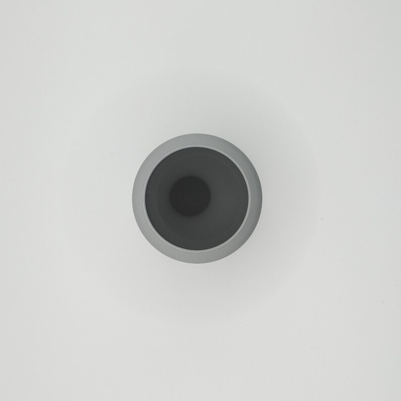 May include: A top-down view of a gray ceramic vase with a dark gray interior. The vase has a rounded shape with a wide opening and a smooth, matte finish. The background is plain white.