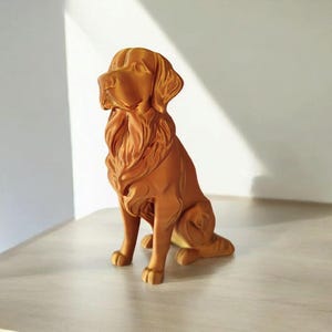 May include: A detailed, brown dog statue in a seated position. The sculpture has a textured surface and intricate details, including the dog's fur and facial features. The statue is placed on a light-colored surface.