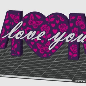 May include: A 3D decorative sign spelling "MOM" with a heart-shaped "O". The letters and heart are purple with pink butterfly and rose patterns. The words "love you" are in white script across the heart.