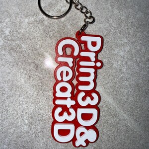 May include: A red and white keychain with the text "Prim3D & Create3D". The keychain has a silver keyring and chain. The text is in a bold, sans-serif font.