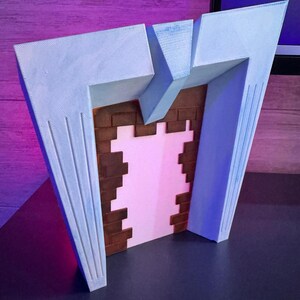 May include: A 3D-printed model of a stylized fireplace. The structure features a light blue facade with vertical grooves, framing a pink interior and a brick-patterned back. The design has a retro, art deco aesthetic.