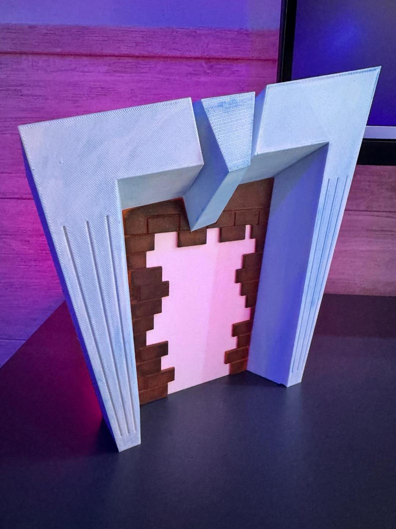 May include: A 3D-printed model of a stylized fireplace. The structure features a light blue facade with vertical grooves, framing a pink interior and a brick-patterned back. The design has a retro, art deco aesthetic.