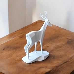 Puede incluir: Una escultura de ciervo geom&eacute;trico blanco con cuernos, de pie sobre una base blanca. El ciervo est&aacute; colocado sobre una superficie de madera, mostrando un dise&ntilde;o moderno y minimalista. Esta pieza decorativa a&ntilde;ade un toque de arte inspirado en la naturaleza.