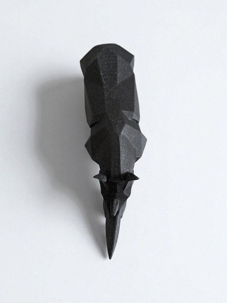 May include: A black, geometric rhino head sculpture. The rhino head is made of a matte black material and features a faceted design. The sculpture is displayed against a white background.
