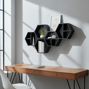 May include: Black hexagonal wall shelves with a small plant, books, and headphones. The shelves are mounted on a light grey wall above a wooden desk with a laptop. The desk is made of wood.