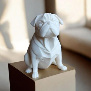 K&ouml;nnte beinhalten: Eine wei&szlig;e Keramik-Mops-Figur mit geometrischem Design. Der Mops sitzt auf einer quadratischen, hellbraunen Box. Die Figur hat detaillierte Gesichtsz&uuml;ge und ist ein dekorativer Gegenstand.
