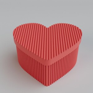 Pu&ograve; includere: Una scatola a forma di cuore color corallo con un design strutturato e scanalato. La scatola ha un coperchio ed &egrave; posta su uno sfondo grigio chiaro. &Egrave; un oggetto decorativo.