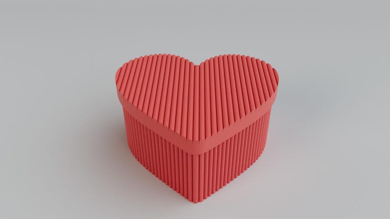 Pu&ograve; includere: Una scatola a forma di cuore color corallo con un design strutturato e scanalato. La scatola ha un coperchio ed &egrave; posta su uno sfondo grigio chiaro. &Egrave; un oggetto decorativo.