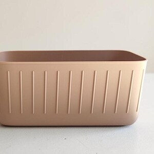 May include: A rectangular, light brown storage bin with vertical grooves on the sides. The bin has a smooth, rounded top edge and a solid, neutral color, suitable for organizing various items.
