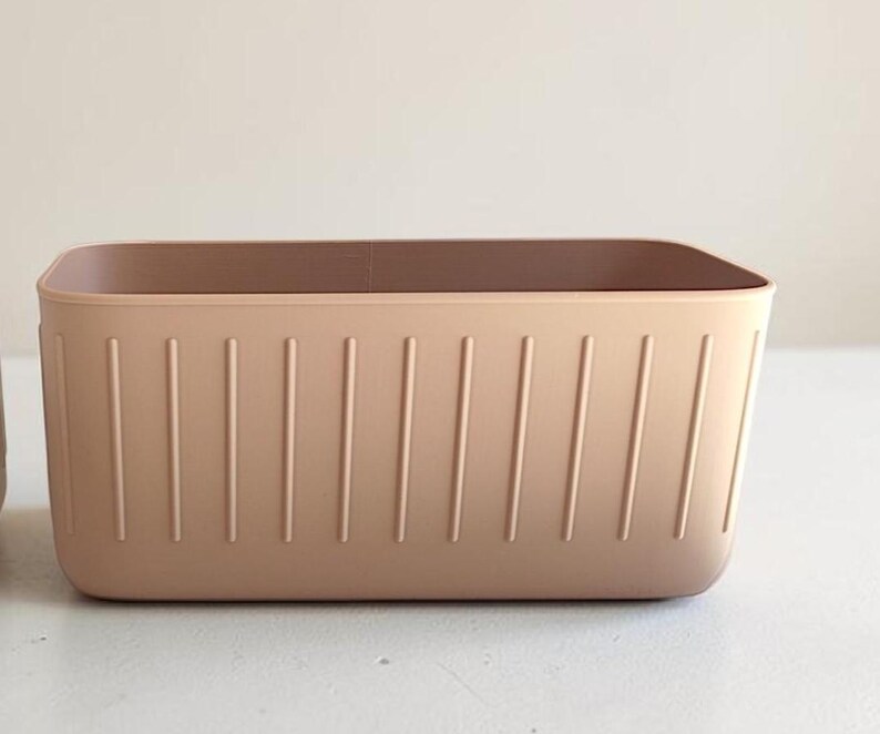 May include: A rectangular, light brown storage bin with vertical grooves on the sides. The bin has a smooth, rounded top edge and a solid, neutral color, suitable for organizing various items.