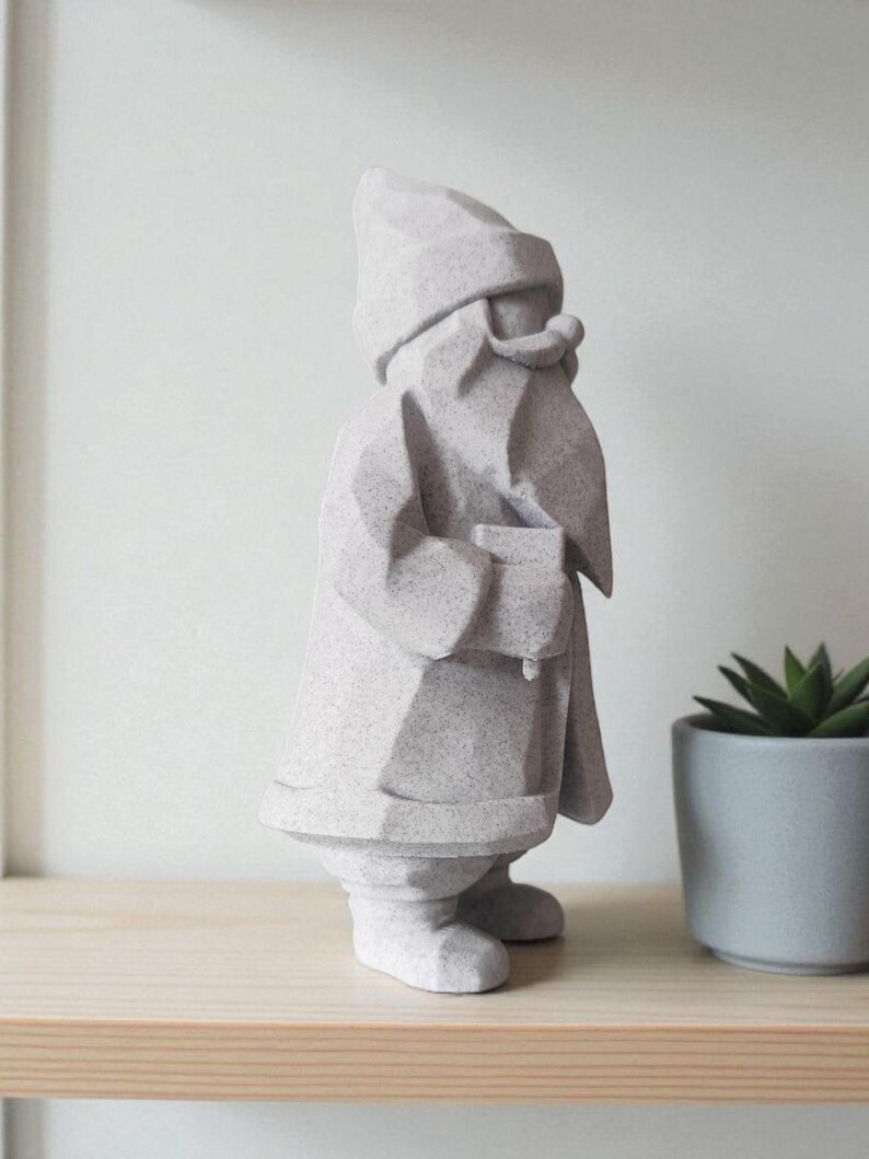 K&ouml;nnte beinhalten: Eine hellgraue geometrische Gartenzwerg-Statue. Der Zwerg tr&auml;gt einen Hut und einen Mantel und hat einen langen Bart. Die Statue steht auf einem Holzregal neben einer kleinen Topfpflanze. Der Zwerg ist ein dekorativer Artikel.