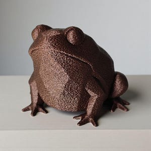 May include: A brown frog figurine with a textured surface. The frog is in a seated position with its front legs extended. The figurine has a detailed, realistic appearance, with visible skin texture and facial features. The frog is a decorative item.