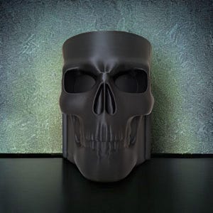 May include: A black skull-shaped decorative container. The container is made of a matte black material and features detailed facial features, including eye sockets, a nose cavity, and teeth. The container is designed to stand upright.