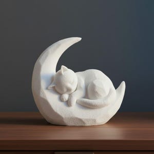 Peut inclure: Figurine blanche repr&eacute;sentant un chat endormi sur un croissant de lune. Le chat est recroquevill&eacute;, les yeux ferm&eacute;s et les pattes repli&eacute;es. La lune a une surface textur&eacute;e et facett&eacute;e, pos&eacute;e sur une surface en bois.