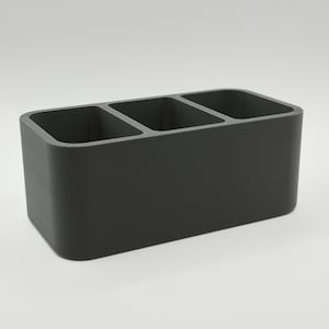May include: A dark gray rectangular organizer with three equally sized compartments. The organizer is made of a solid material and has rounded corners. It is designed for desk or counter organization.