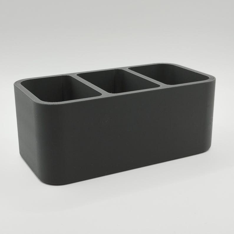 May include: A dark gray rectangular organizer with three equally sized compartments. The organizer is made of a solid material and has rounded corners. It is designed for desk or counter organization.