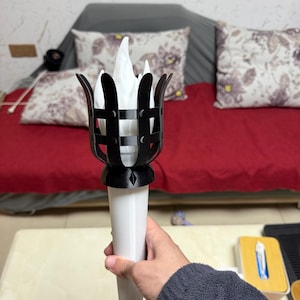 May include: A decorative torch with a black cage-like top and a white handle. The torch features a stylized flame design. The flame appears to be made of white fabric or paper.