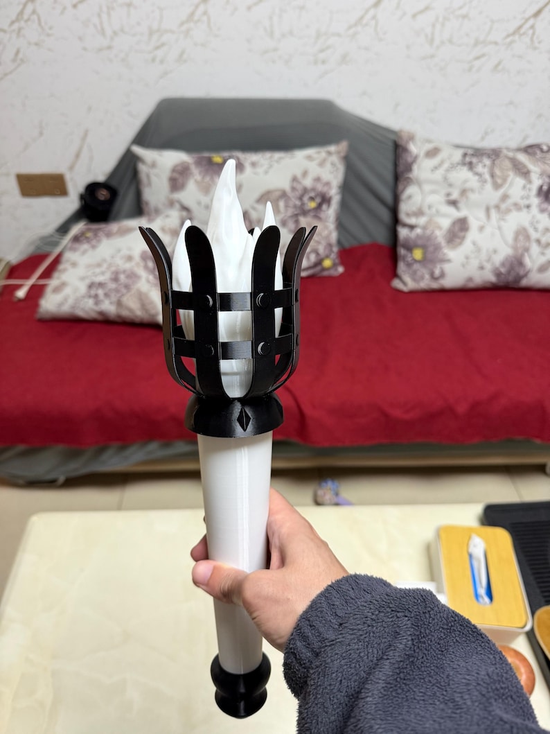 May include: A decorative torch with a black cage-like top and a white handle. The torch features a stylized flame design. The flame appears to be made of white fabric or paper.