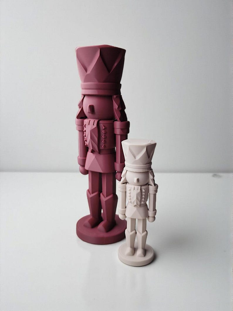 May include: Two decorative nutcrackers in a minimalist style. One is a larger, deep burgundy color, and the other is smaller and a light beige. Both have a geometric design and stand on round bases. The nutcrackers are a festive holiday decoration.