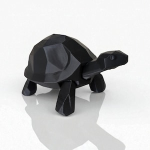 May include: A black, geometric-style turtle figurine. The sculpture has a faceted shell and a smooth, elongated head. The turtle is standing on four blocky legs. The figurine is made of a solid, dark material and casts a shadow.
