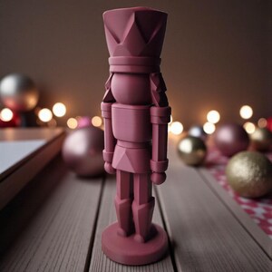 May include: A maroon-colored nutcracker figurine with a crown and soldier-like attire. The figurine is standing on a round base. Christmas ornaments and soft bokeh lights are in the background, suggesting a holiday theme.