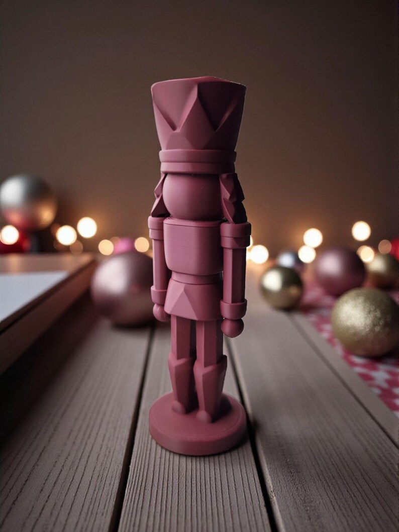 May include: A maroon-colored nutcracker figurine with a crown and soldier-like attire. The figurine is standing on a round base. Christmas ornaments and soft bokeh lights are in the background, suggesting a holiday theme.