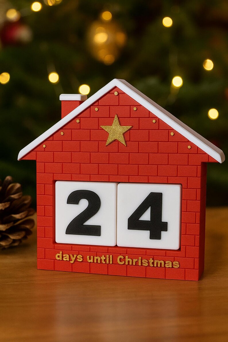 May include: A red house-shaped Christmas countdown calendar with a white roof and a gold star. The calendar displays the number 24 on white blocks, with the text "days until Christmas" below.