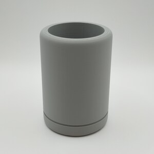 May include: A cylindrical, gray tumbler with a wide opening. The tumbler has a smooth, matte finish and a slightly rounded base. The design is simple and modern, suitable for holding beverages. The tumbler is approximately 5 inches tall.