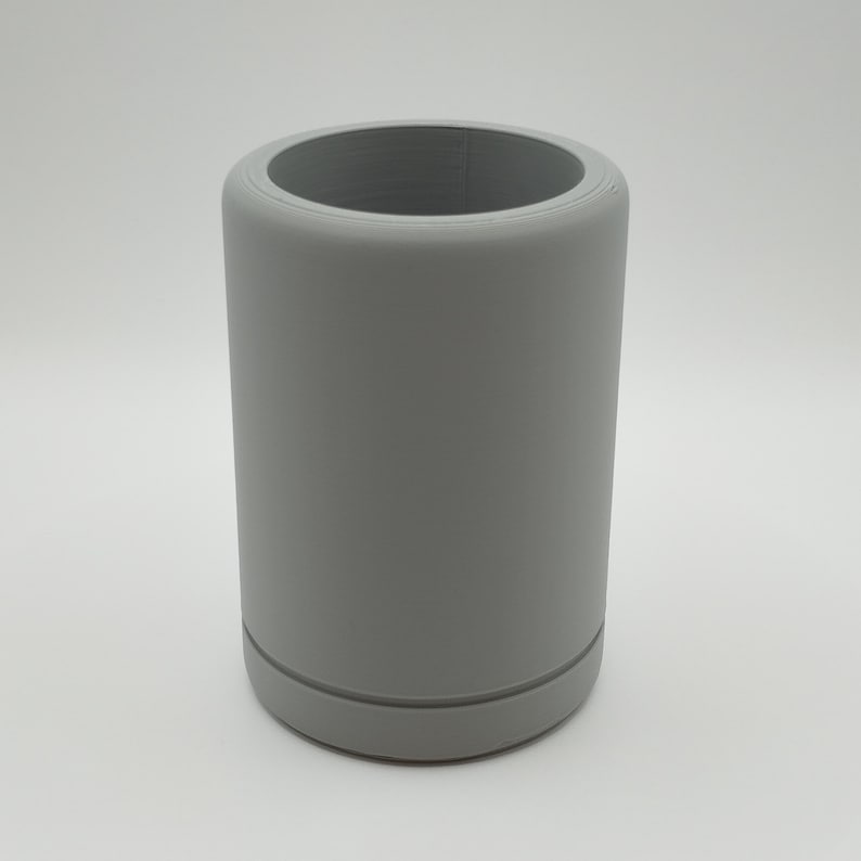 May include: A cylindrical, gray tumbler with a wide opening. The tumbler has a smooth, matte finish and a slightly rounded base. The design is simple and modern, suitable for holding beverages. The tumbler is approximately 5 inches tall.