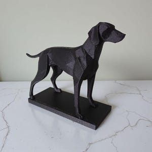 May include: A black geometric dog sculpture. The dog stands on a rectangular base. The sculpture has a modern, angular design and is made of a solid, dark material.