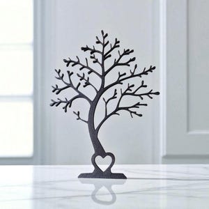 May include: A black metal tree-shaped jewelry holder with a heart cutout. The tree has many branches and sits on a rectangular base. The jewelry holder is displayed on a white surface.