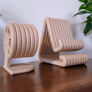 Puede incluir: Dos organizadores de escritorio de madera de color beige claro. Uno es un soporte para tel&eacute;fono con un dise&ntilde;o de listones, y el otro es un soporte redondo con un recorte en forma de estrella. Ambos son de madera.