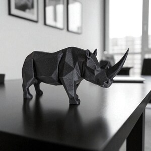 May include: A black, geometric rhino sculpture with a prominent horn. The rhino is positioned on a black table, showcasing its angular design. The sculpture is a modern decorative piece, suitable for home or office decor.