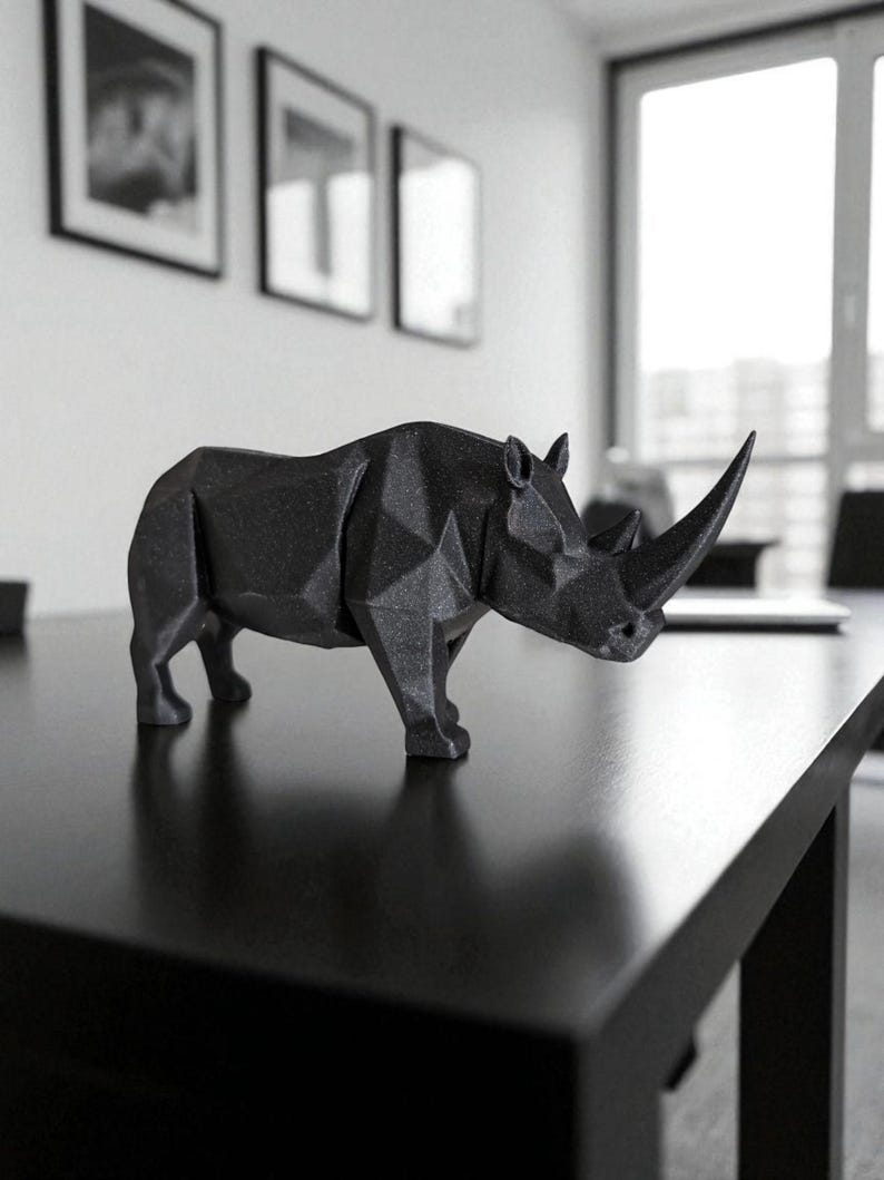 May include: A black, geometric rhino sculpture with a prominent horn. The rhino is positioned on a black table, showcasing its angular design. The sculpture is a modern decorative piece, suitable for home or office decor.