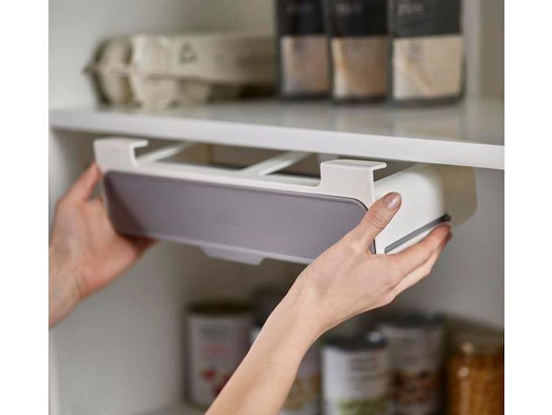 May include: A white and gray under-shelf drawer being installed in a kitchen cabinet. The drawer has a gray front and is held by a person's hands. The cabinet shelf above has a carton of eggs and spice jars.