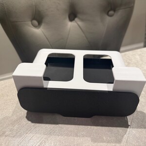 May include: A white and black desk organizer with a rectangular shape. The organizer has two open compartments and a black front panel. The design is modern and minimalist, suitable for office or home use.