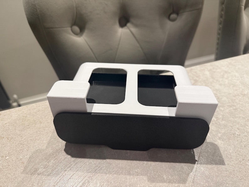 May include: A white and black desk organizer with a rectangular shape. The organizer has two open compartments and a black front panel. The design is modern and minimalist, suitable for office or home use.