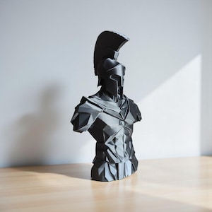 May include: A dark grey bust of a Spartan warrior, with a helmet and a high crest, and detailed armour. The sculpture is set against a neutral background, highlighting the geometric design and form of the ancient Greek figure.